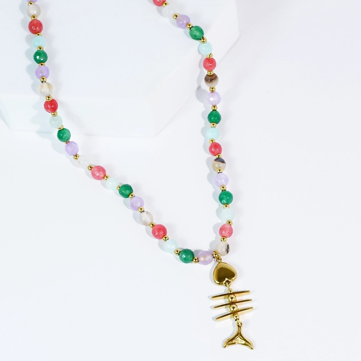 a beaded necklace with a fishbone gold pendant on a white background. 