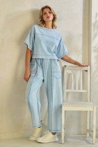 Woman wearing a light blue outfit standing next to a white chair against a beige wall.