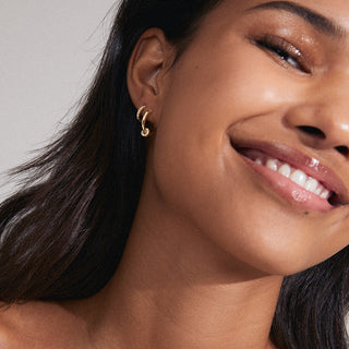 Close-up of a woman wearing gold hoop earrings with a neutral background