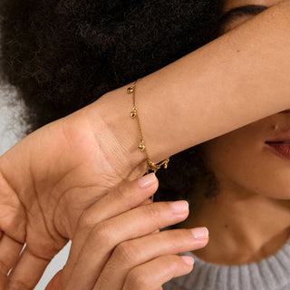 Close-up of a person wearing a gold bracelet on a neutral background