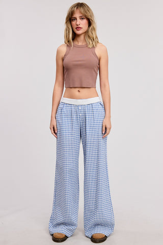 Woman wearing a brown sleeveless top and blue checkered pants on a light gray background