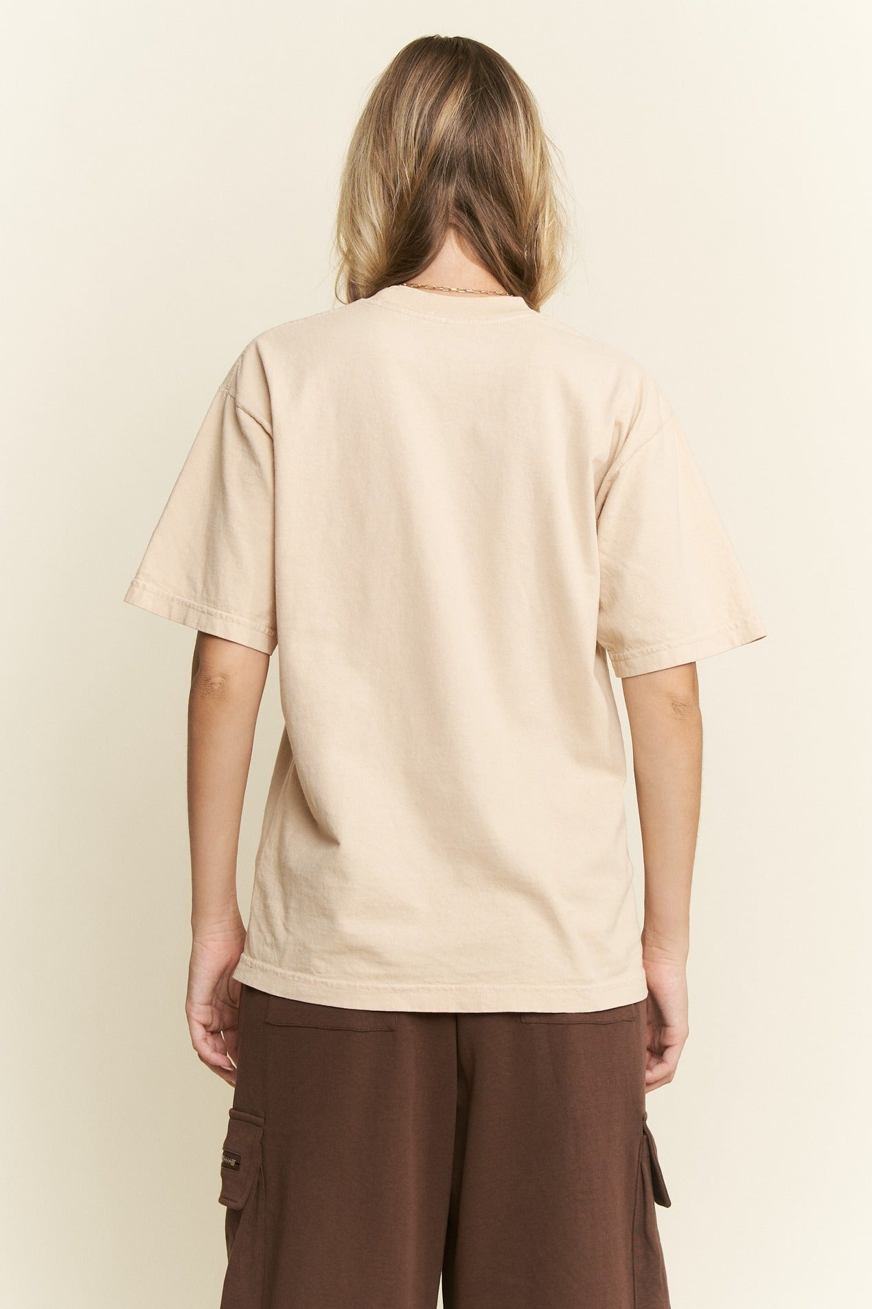Person wearing a beige t-shirt and brown pants on a plain background