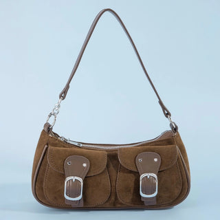 A brown suede shoulder bag with two front flap pockets, each featuring a brown leather strap and silver buckle, on a light blue background.
