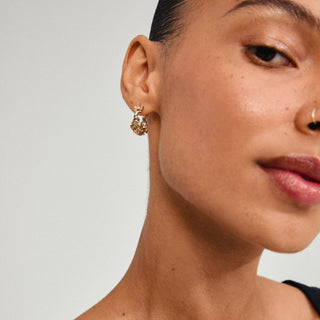 Close-up of a person wearing gold hoop earrings with a neutral background