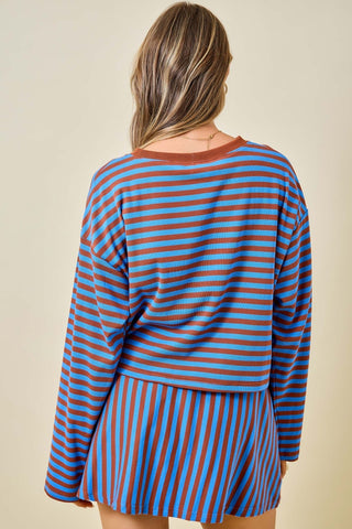 A woman viewed from behind wearing a matching long-sleeve top and skirt set with horizontal blue and rust-orange stripes, against a plain beige background.