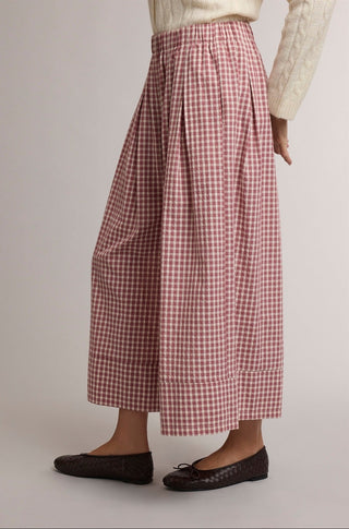 A person wearing high-waisted, wide-leg cropped pants in a red and white gingham pattern, styled with a cream knit top and dark brown flat shoes against a neutral studio background.