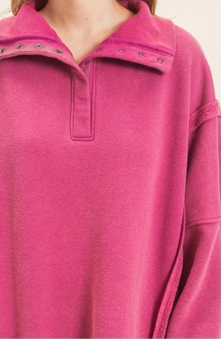 A close-up of a person wearing a bright pink long-sleeve quarter-placket top with metal grommet details along the collar.