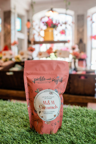 Pink package of M&M Caramels on a grassy surface with a blurred indoor background