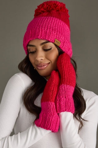Woman wearing a pink knit hat and scarf with a brown pom-pom against a gray background