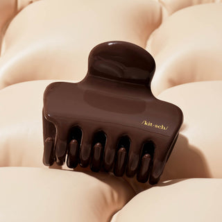 Brown hair clip with 'kitsch' branding on a beige textured background