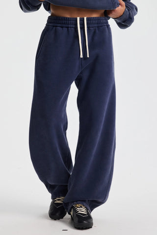 A person wearing navy wide-leg sweatpants with white drawstrings, paired with black sneakers, shown from the waist down against a light gray studio background.