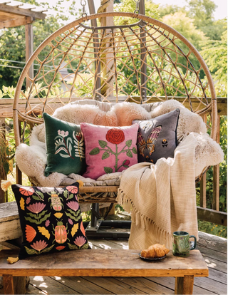 Wicker chair with decorative pillows and a blanket on a wooden deck