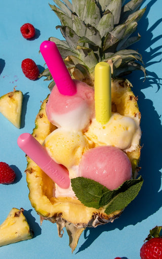 Pineapple boat filled with colorful ice cream and fruit on a blue background featuring three lip balms