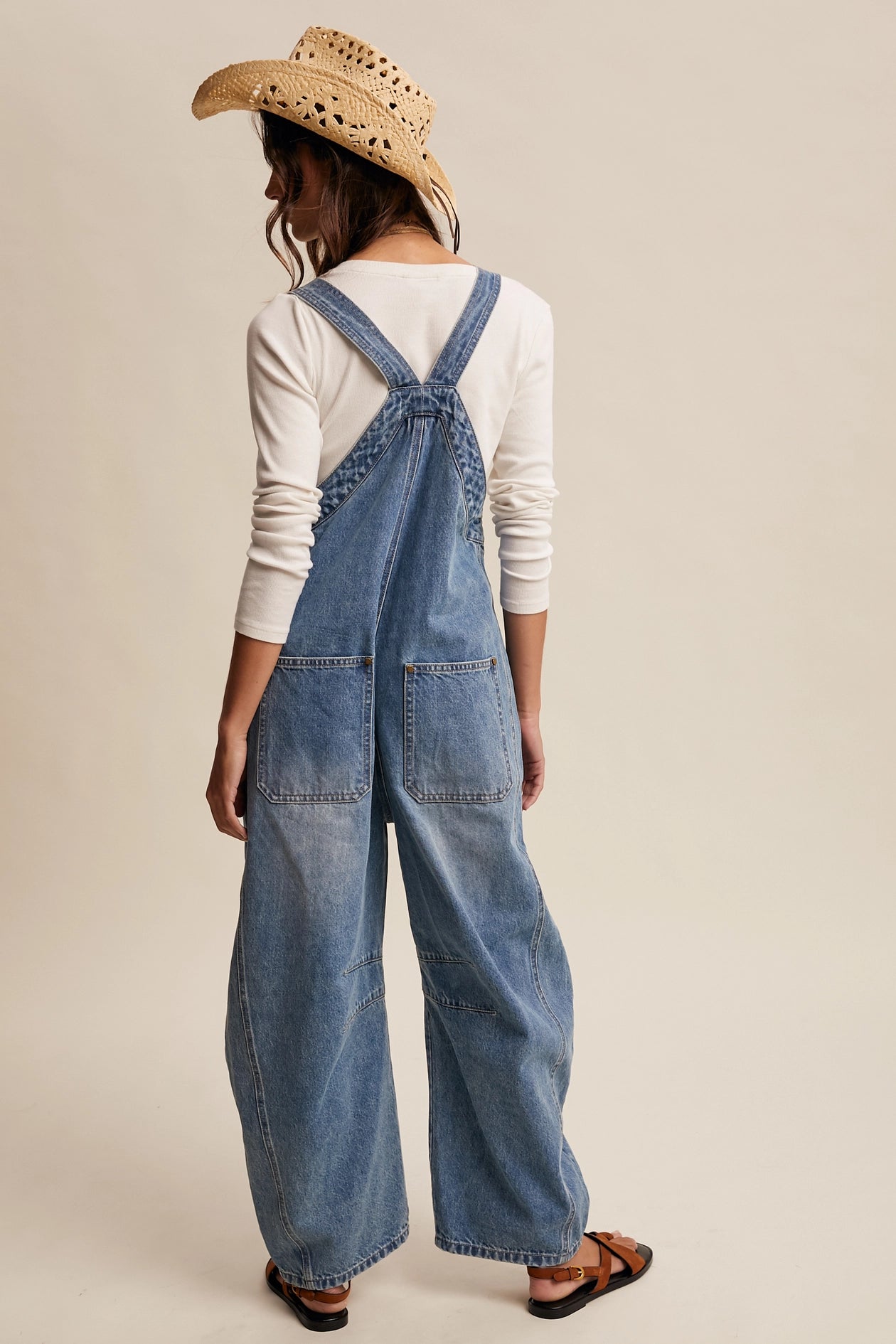 Person wearing blue denim overalls and a straw hat on a beige background