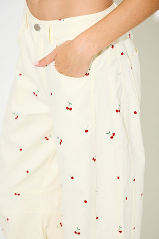 White pants with red cherry pattern worn by a person on a plain background