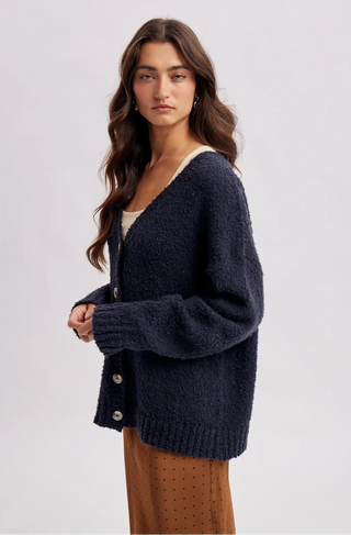 Women wearing a navy cardigan against a neutral background.