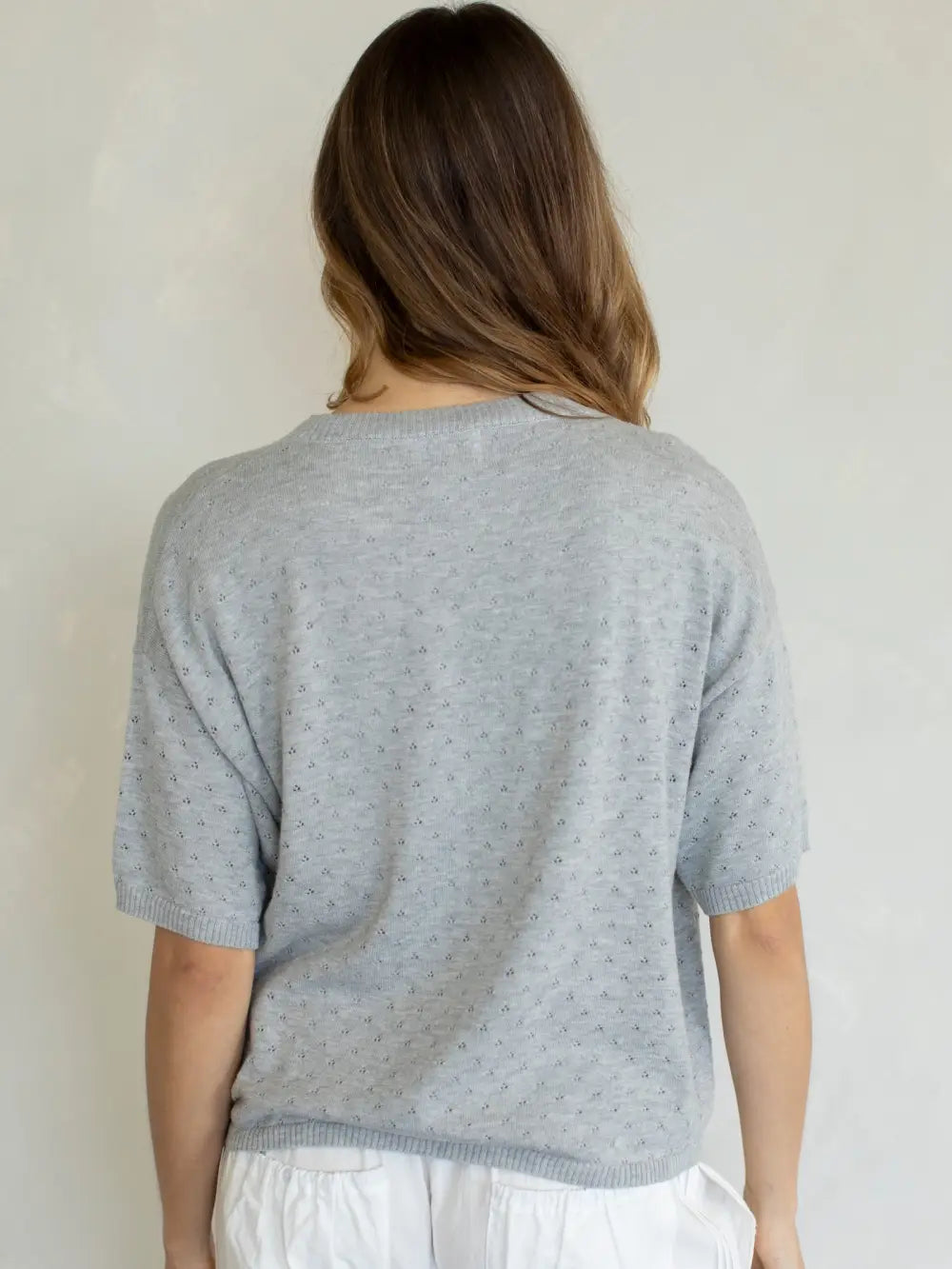 Person wearing a light gray short-sleeve sweater against a plain background