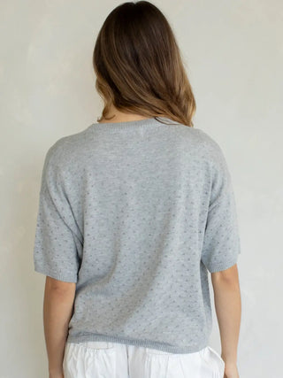 Person wearing a light gray short-sleeve sweater against a plain background