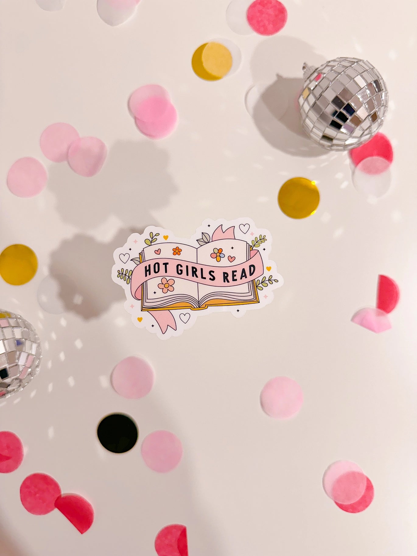 Sticker with 'Hot Girls Read' design on a surface with confetti and disco balls.