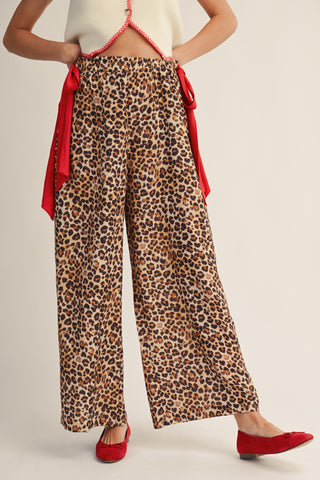 Person wearing leopard print pants with a red top and shoes on a plain background