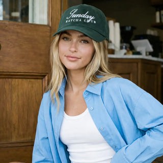 Woman wearing a green cap with 'Sundary Matcha Club' text, sitting indoors.