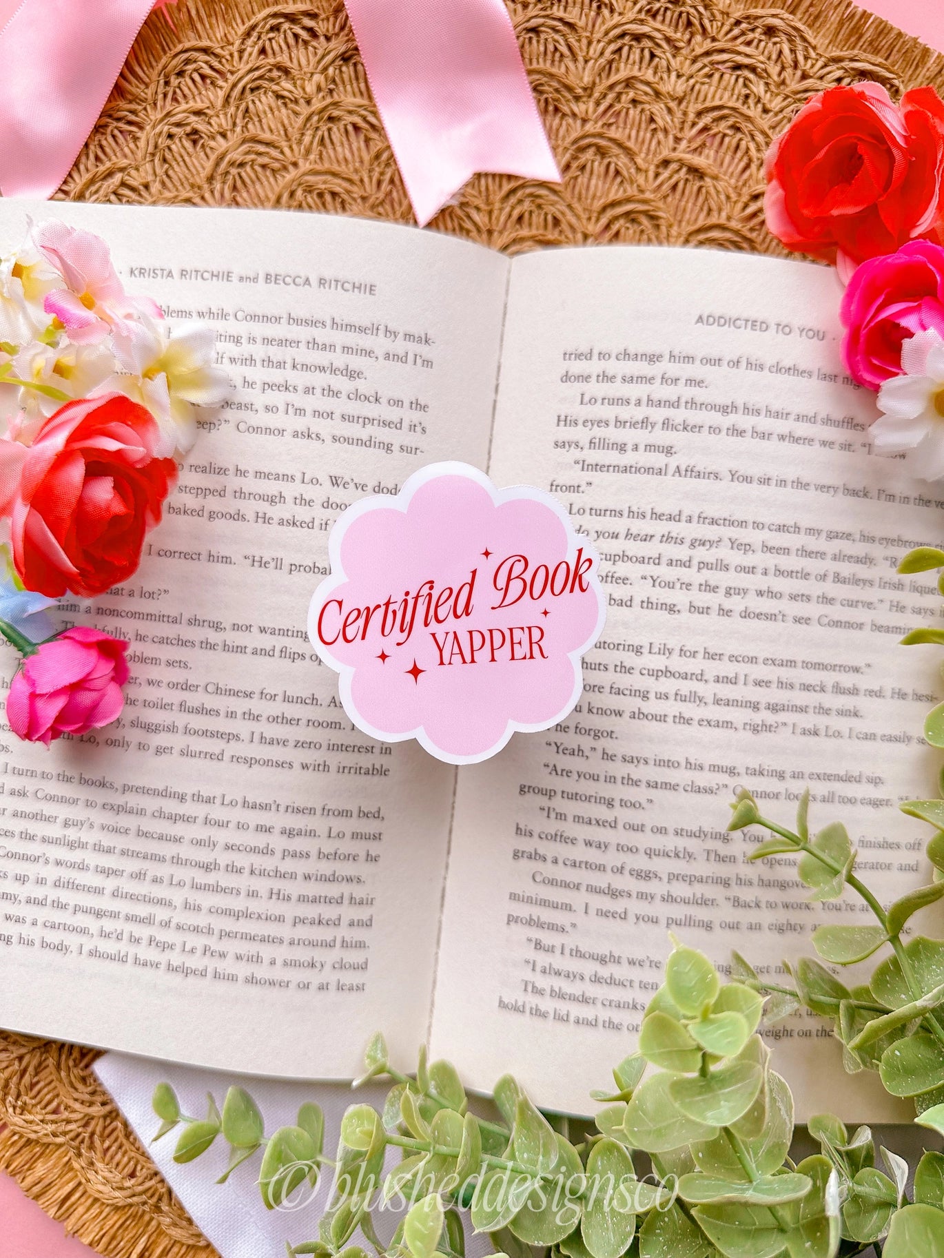 Open book with flowers and a 'Certified Book Yapper' sticker on a textured surface.