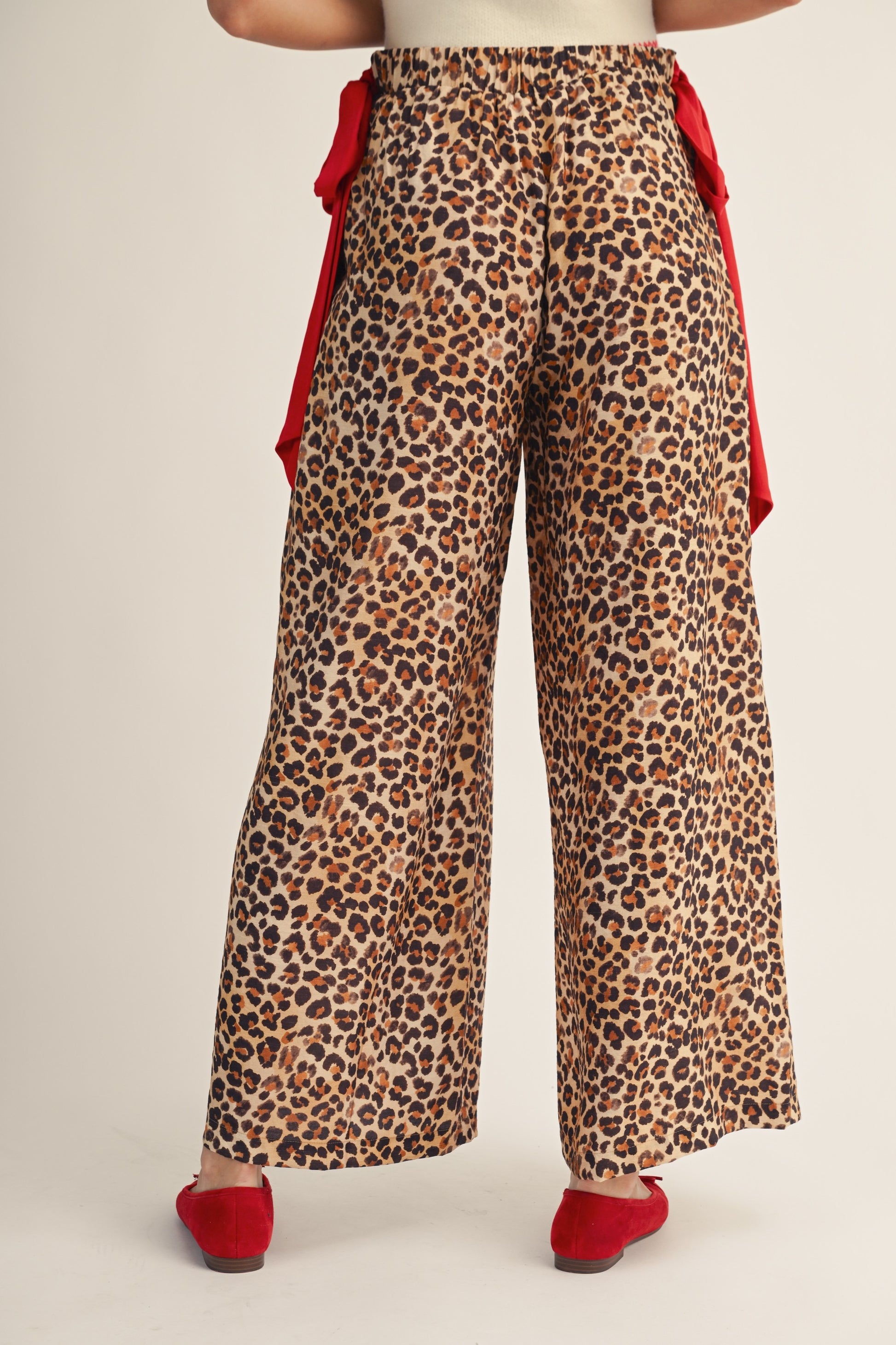 Leopard print pants with red accents worn by a person on a plain background