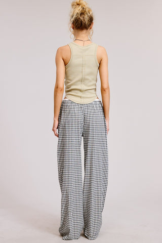 Person wearing a light green sleeveless top and checkered pants on a plain background