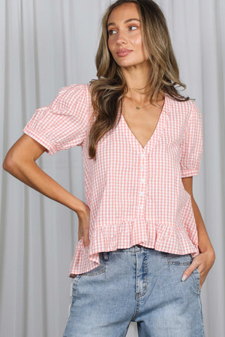 Woman wearing a pink checkered blouse and blue jeans against a light gray background