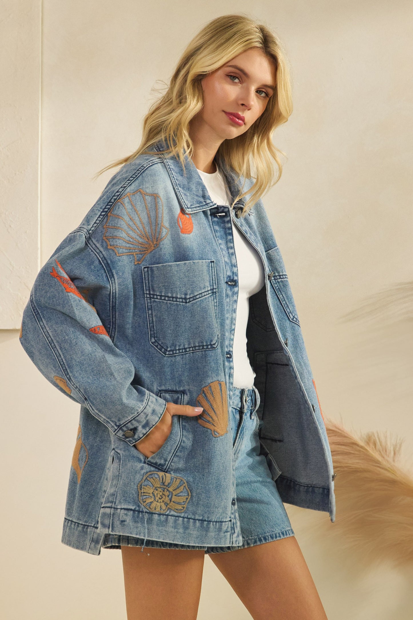 Woman wearing a denim jacket with embroidered sea creatures on a beige background