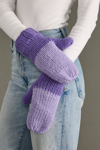 Purple knitted mittens worn by a person with a white sweater and blue jeans.