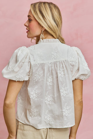 Woman wearing a white embroidered blouse with puff sleeves against a pink background