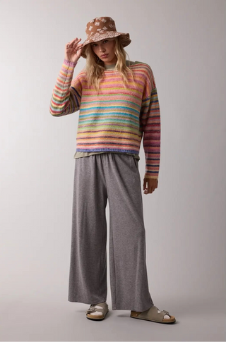A women wearing a rainbow sweater against a neutral background.