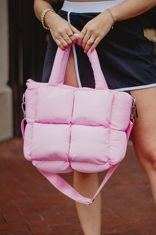 Person holding a pink quilted bag with a blurred background