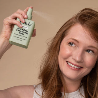 Woman holding a bottle of root lifting and thickening spray against a beige background