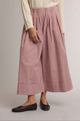 A model wearing a pair of high-waisted, wide-leg cropped pants in a red and white gingham check pattern, styled with a cream cable-knit long-sleeve top and dark brown flat shoes against a neutral studio background.