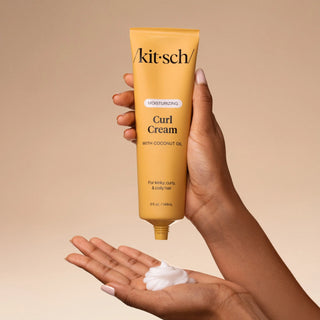 Hand holding a tube of 'kitsch' Curl Cream with coconut oil against a beige background