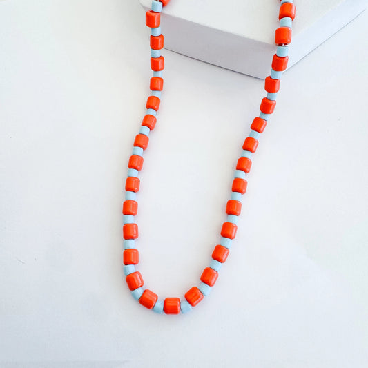 An orange and blue beaded necklace on a plain background. 