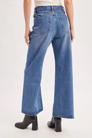 A person shown from the back wearing blue wide-leg jeans and black heeled ankle boots against a plain light background.