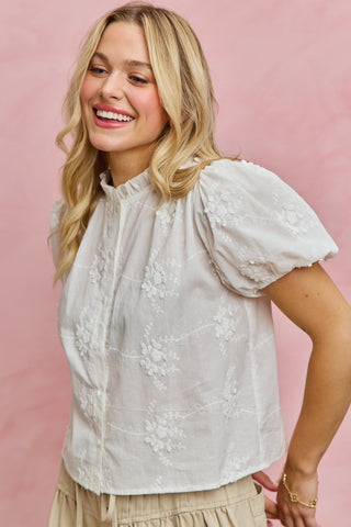 Woman wearing a white blouse with floral embroidery against a pink background