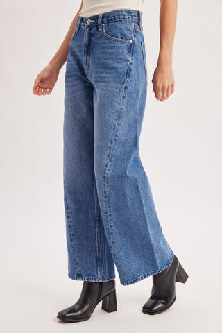 A person wearing high-waisted, wide-leg blue denim jeans with black heeled ankle boots, shown from the waist down against a plain light background.