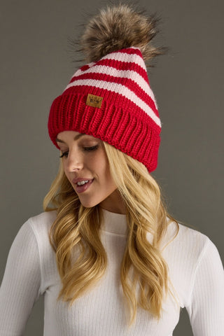 Red and white striped knit beanie with fur pom-pom worn by a person against a gray background