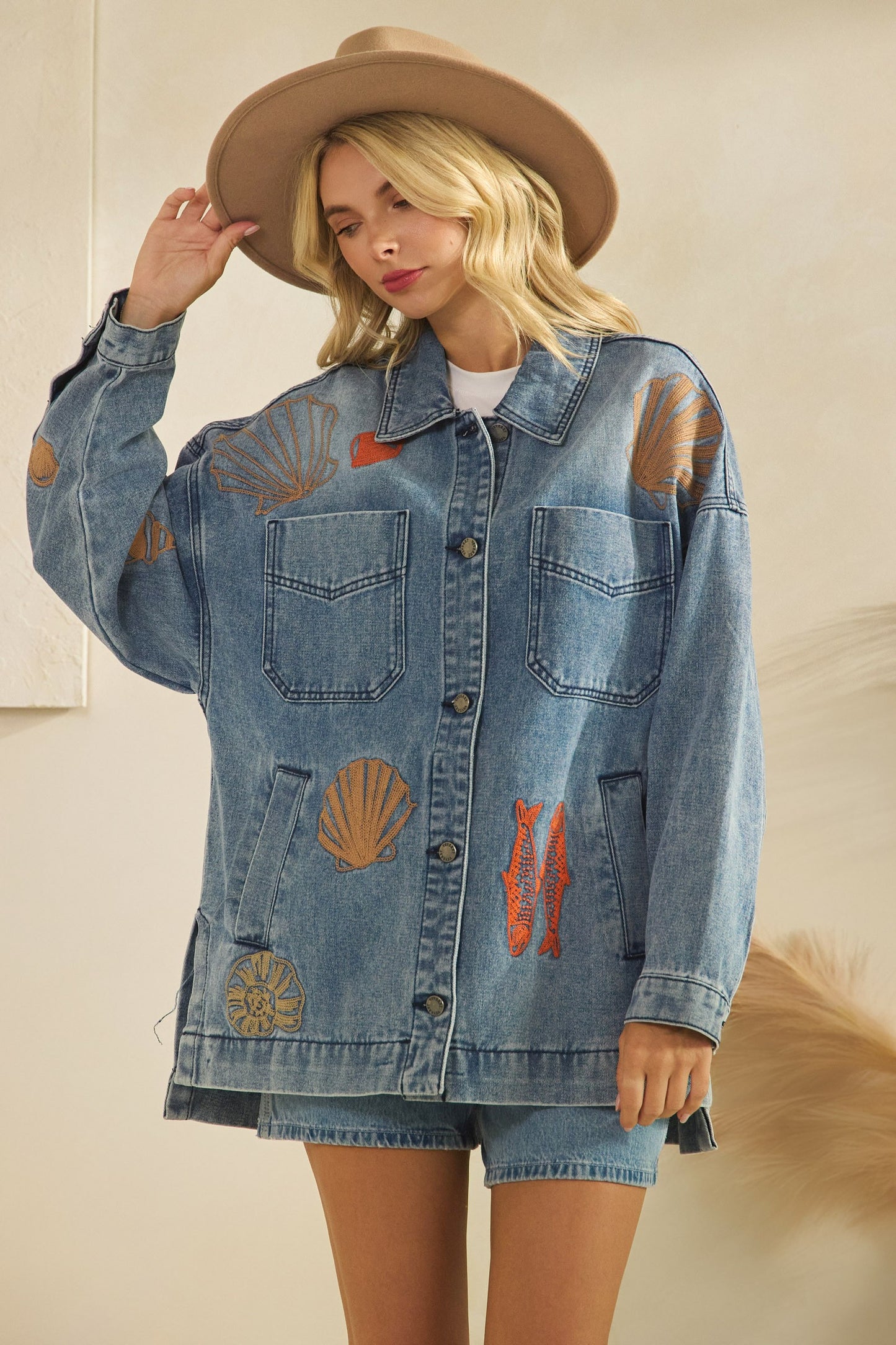 Woman wearing a denim jacket with embroidered sea creatures on a beige background