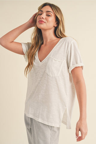 Woman wearing a white V-neck top with a pocket on a beige background