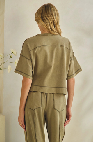 A woman shown from the back wearing a matching cropped short-sleeve top and wide-leg pants set in a muted olive khaki color, featuring contrast stitching details.