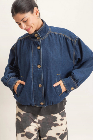 A woman wearing a dark blue denim jacket with a high stand-up collar and front buttons, paired with black and white cow-print pants, photographed against a plain light background.