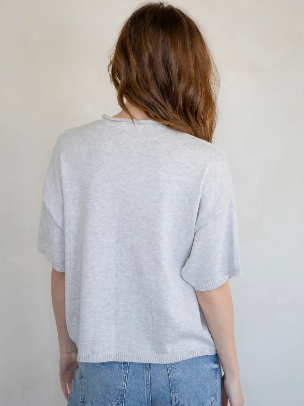 Person wearing a light gray sweater and blue jeans against a plain background