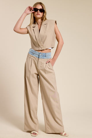 Woman wearing a beige sleeveless top and wide-leg pants with sunglasses on a beige background