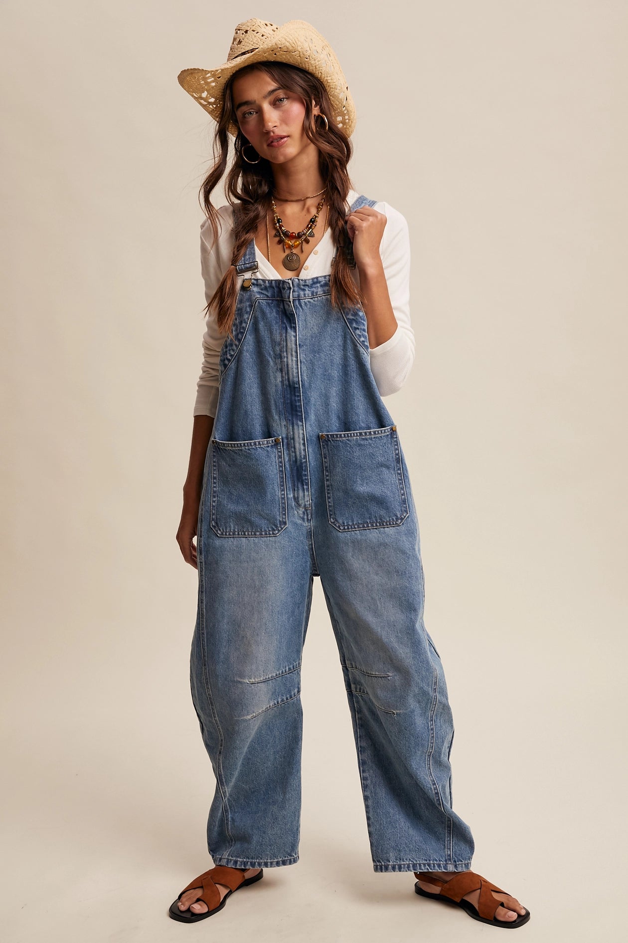 Woman wearing denim overalls and a straw hat on a beige background