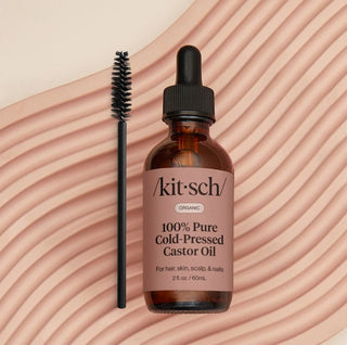 Brown bottle of 'Kitsch' 100% Pure Cold-Pressed Castor Oil with a dropper on a beige background